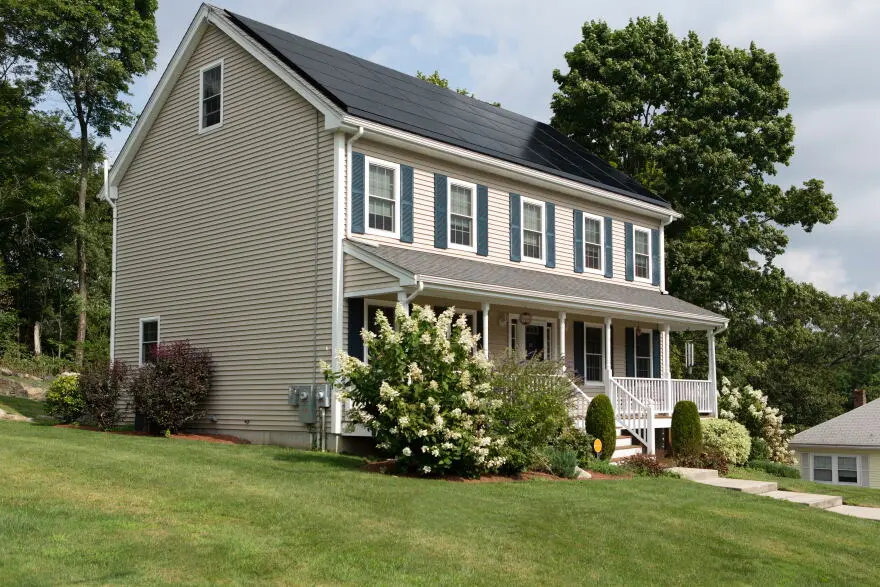 Two-story home with rooftop solar panels, traditional siding, shutters, and a front porch